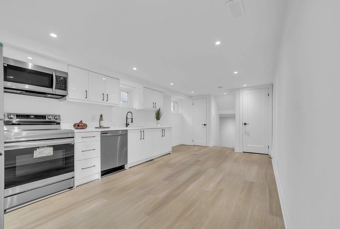 Finished basement with a white kitchenette, pot lights and light oak vinyl plank flooring in Concord, by NewGen Renovations Vaughan
