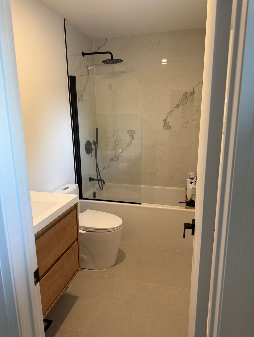 Bathroom with a glass splash panel over the tub, marble-look tile and a floating oak vanity in Concord, by NewGen Renovations Vaughan