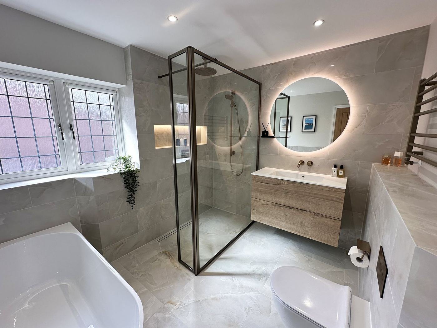 Bathroom renovation with a bronze-framed walk-in shower, backlit round mirror and floating oak vanity by NewGen Renovations Vaughan