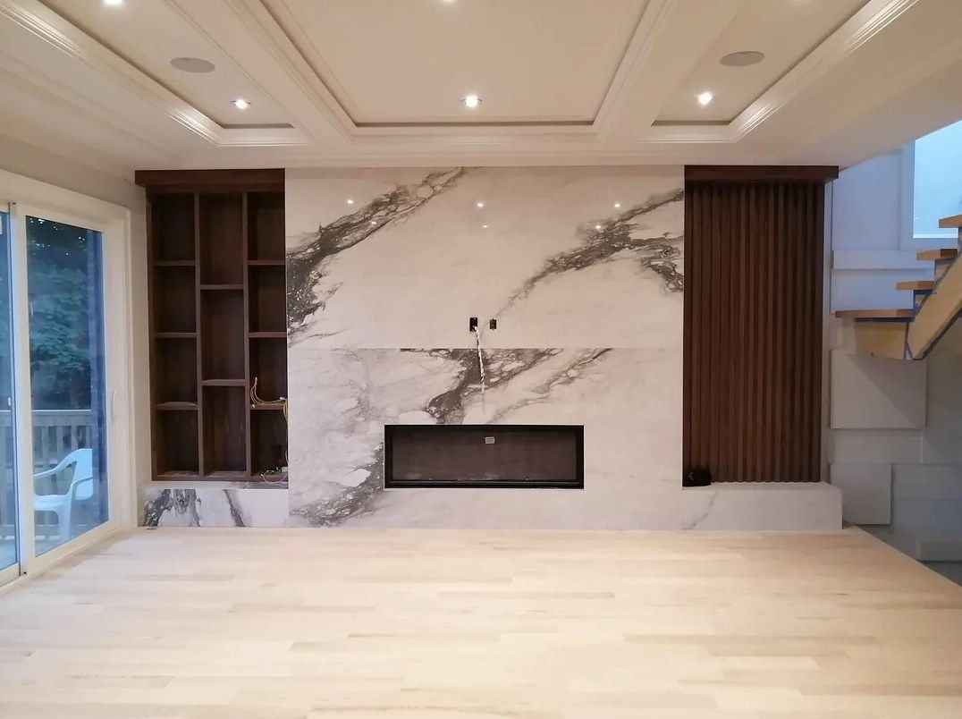 Fireplace feature wall with a linear fireplace set in a marble-look slab, walnut built-in shelving on one side and a walnut slat panel on the other, built by NewGen Renovations Vaughan