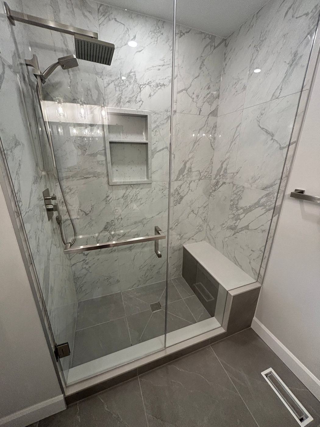 Walk-in glass shower with large marble-look wall tile, a built-in bench, recessed niche and brushed nickel fixtures after a tub-to-shower conversion by NewGen Renovations Vaughan