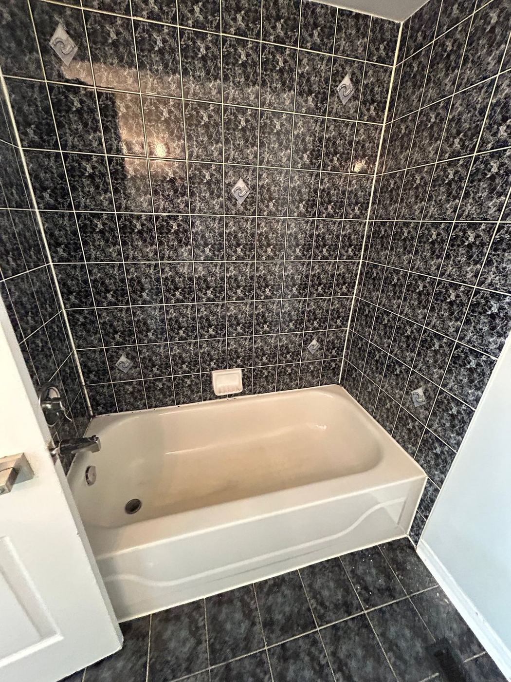 Dated alcove bathtub with glossy black marble-pattern wall tile before a tub-to-shower conversion by NewGen Renovations Vaughan
