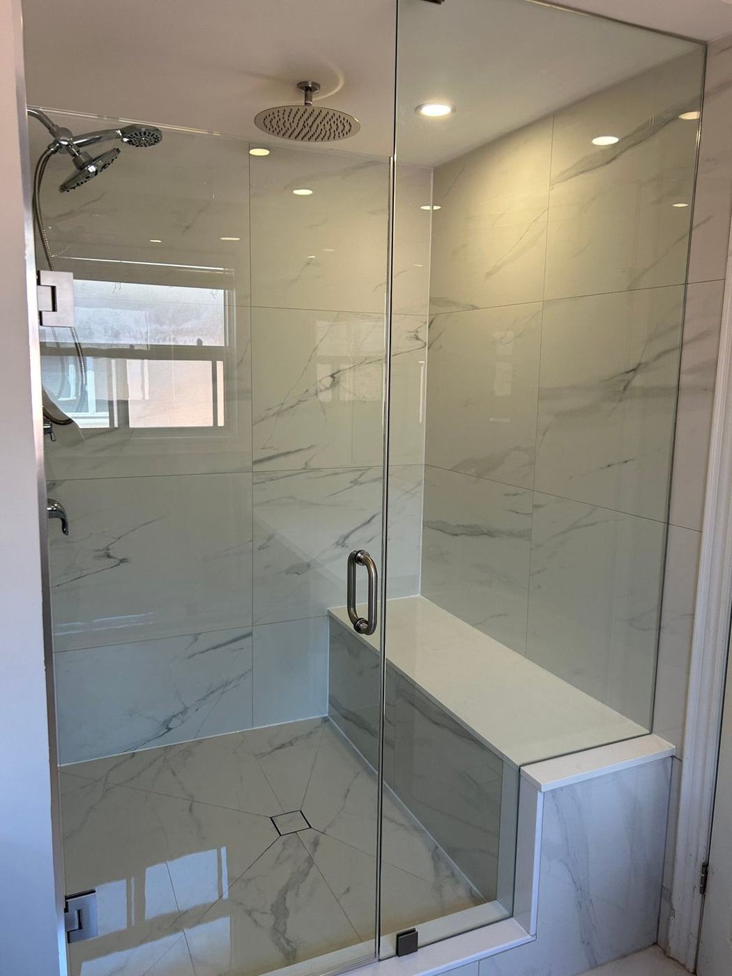 Walk-in shower with a frameless glass enclosure, a built-in quartz-topped bench and large white marble-look tile by NewGen Renovations Vaughan